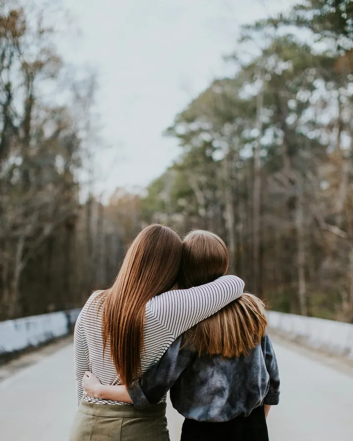 Original photo: two friends with long hair hugging on a quiet road lined with trees